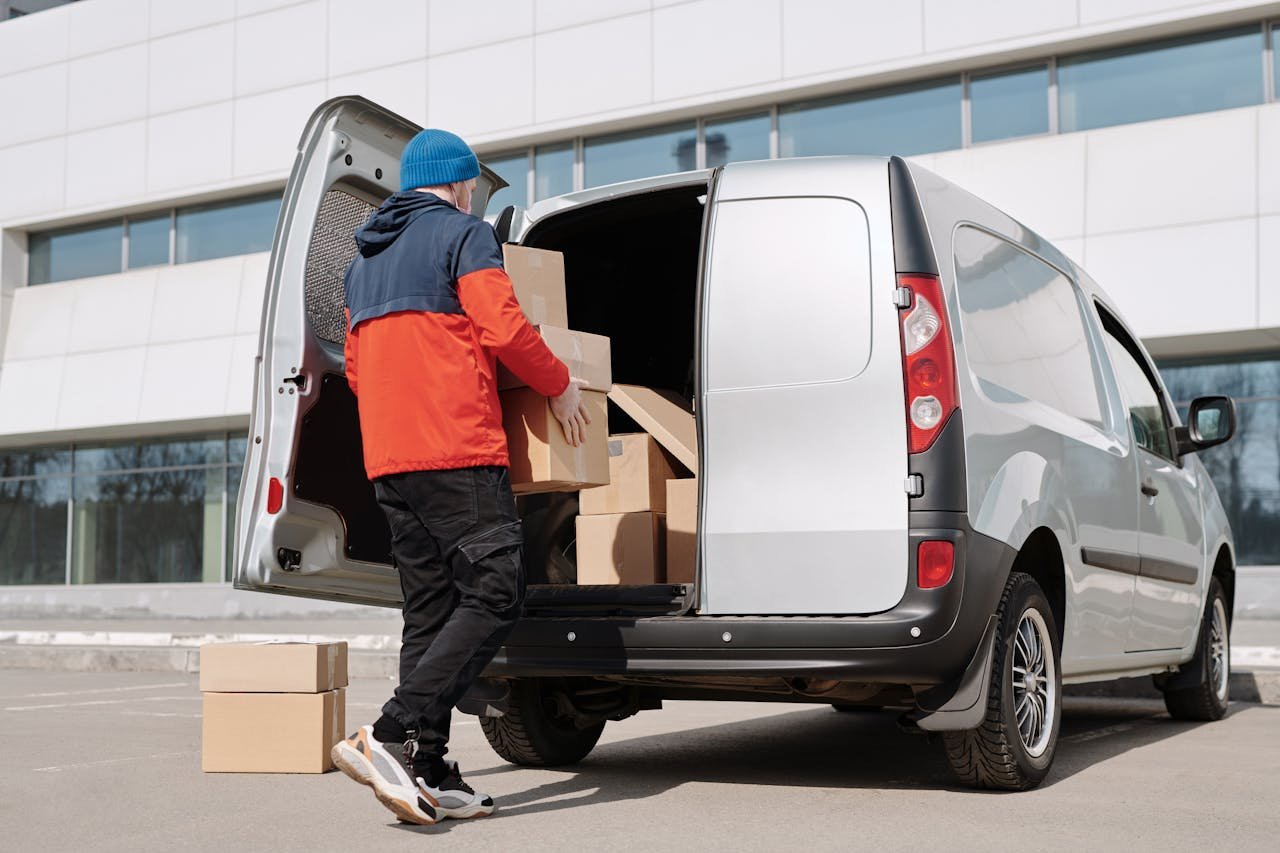 Services Man in colorful jacket loading cardboard boxes into a van outside an office building.
